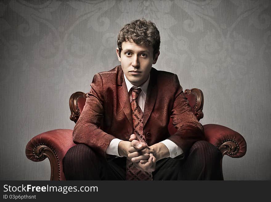 Portrait of a young elegant man sitting on a velvet armchair. Portrait of a young elegant man sitting on a velvet armchair