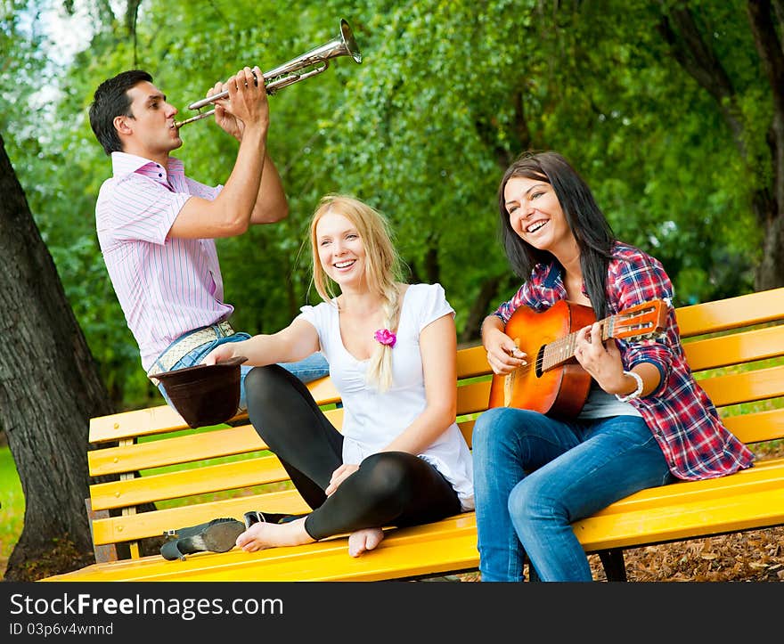 Young friends play the guitar and trumpet in the park