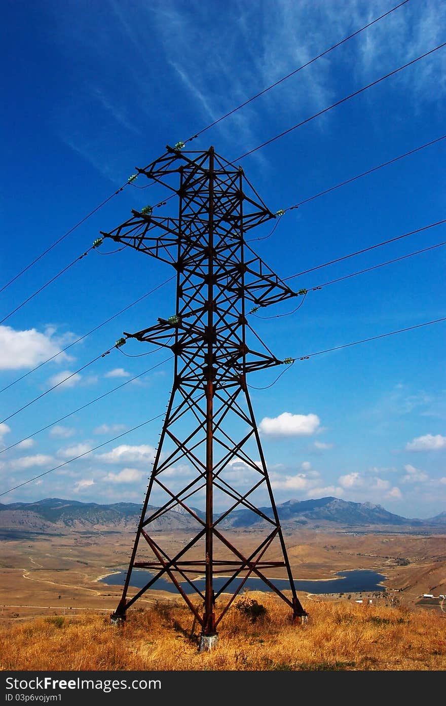 High-voltage line on background with clean blue sky with clouds,mountains and lake behinde. High-voltage line on background with clean blue sky with clouds,mountains and lake behinde