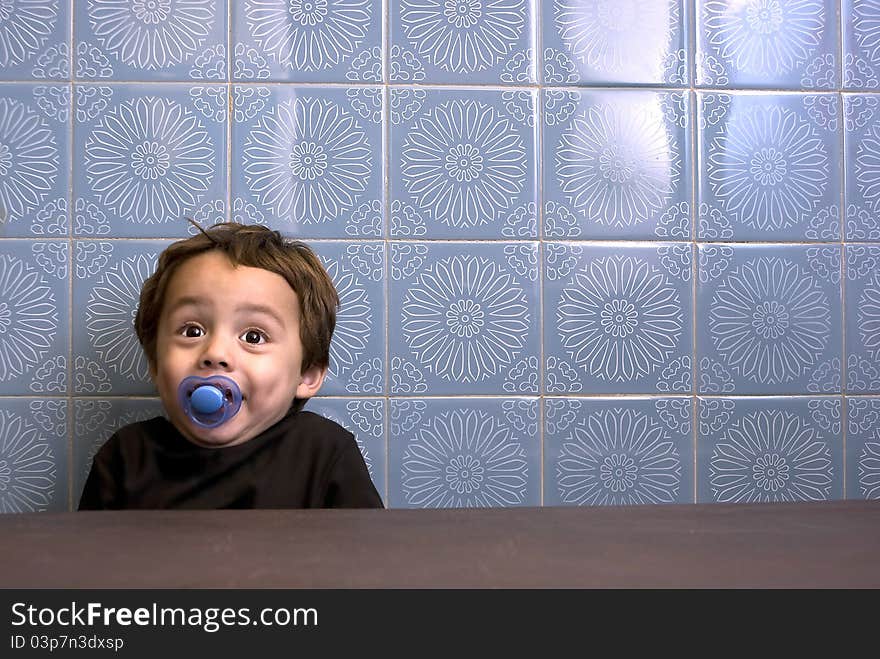 Portrait of a little boy smiling. He is sitting at a table in front of a very retro looking wall. Portrait of a little boy smiling. He is sitting at a table in front of a very retro looking wall.