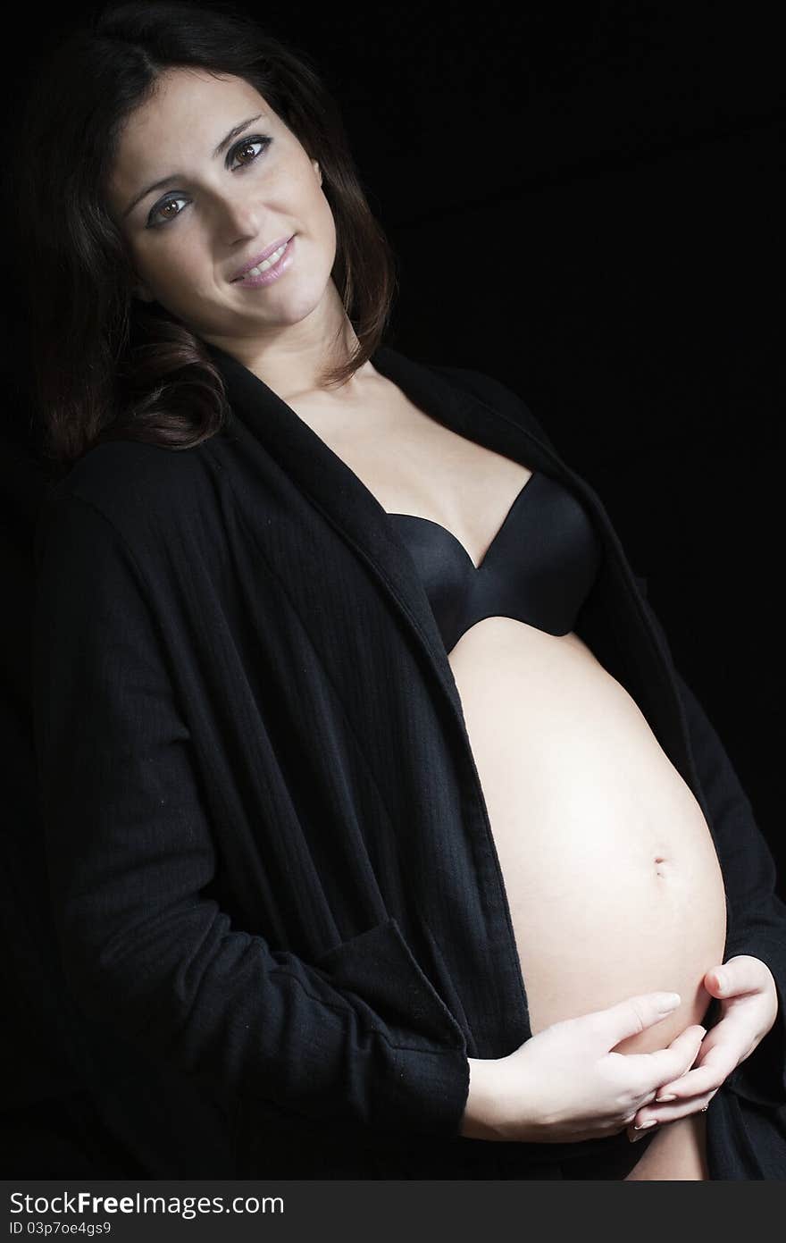 Pregnant woman with a black robe standing on a black background. Pregnant woman with a black robe standing on a black background