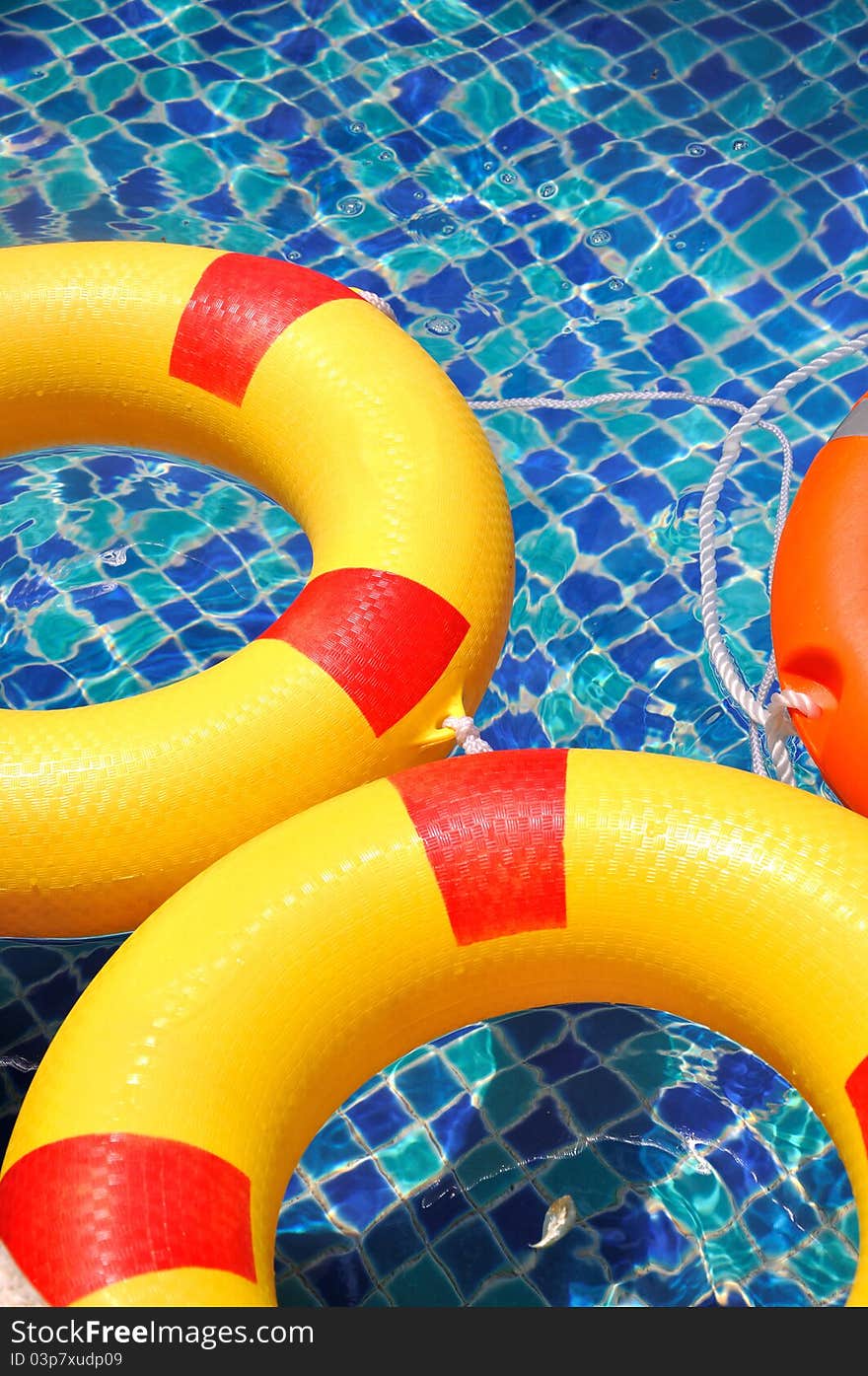 Yellow and red life buoy floating in blue color swimming pool, shown as spare time or holidy enjoying and beautiful color of rings and water. Yellow and red life buoy floating in blue color swimming pool, shown as spare time or holidy enjoying and beautiful color of rings and water.