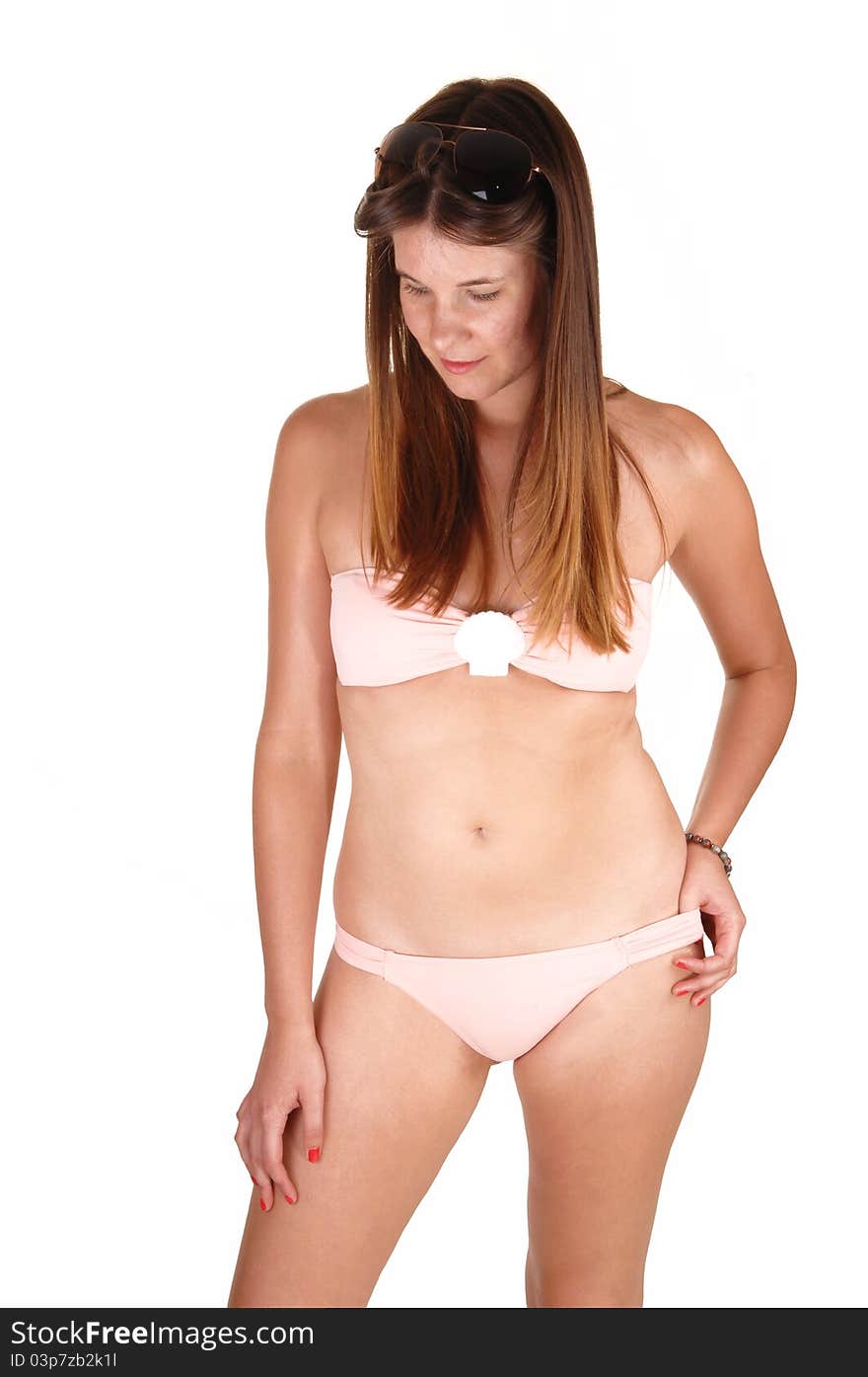 A young girl in a pink bikini standing in the studio with her long brunette hair and looking down on the floor, for white background. A young girl in a pink bikini standing in the studio with her long brunette hair and looking down on the floor, for white background.