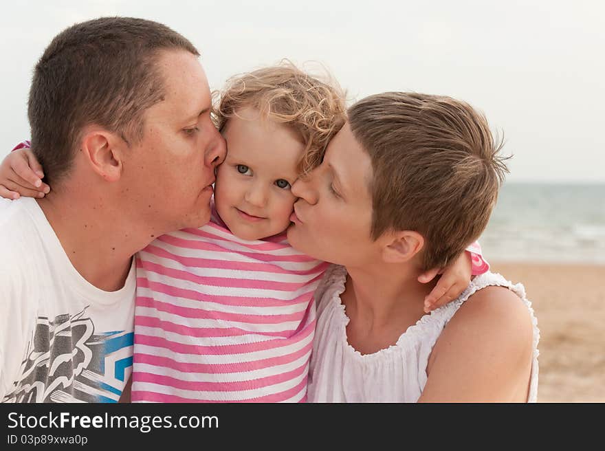 Parents are kissing little baby on beach