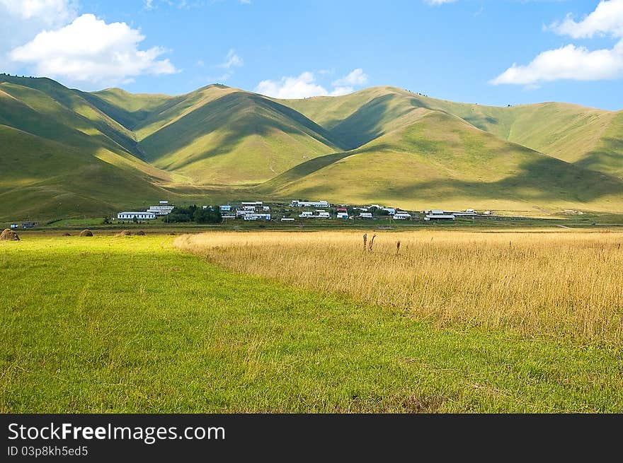 Village at a foot of green mountains under the dark blue sky. Village at a foot of green mountains under the dark blue sky