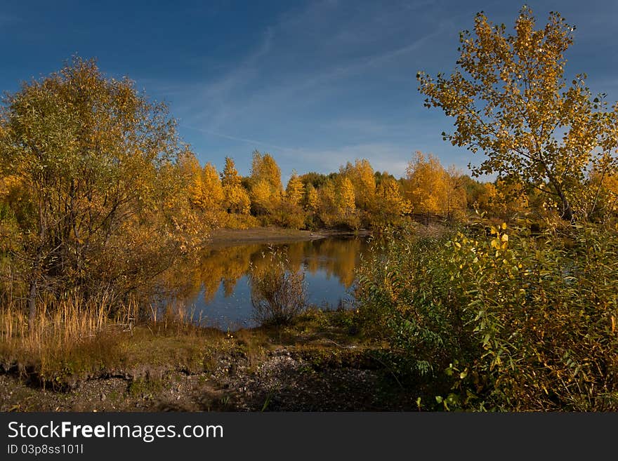 Autumn trees with the turned yellow foliage are reflected in dark blue lake, over them the blue sky. Autumn trees with the turned yellow foliage are reflected in dark blue lake, over them the blue sky.