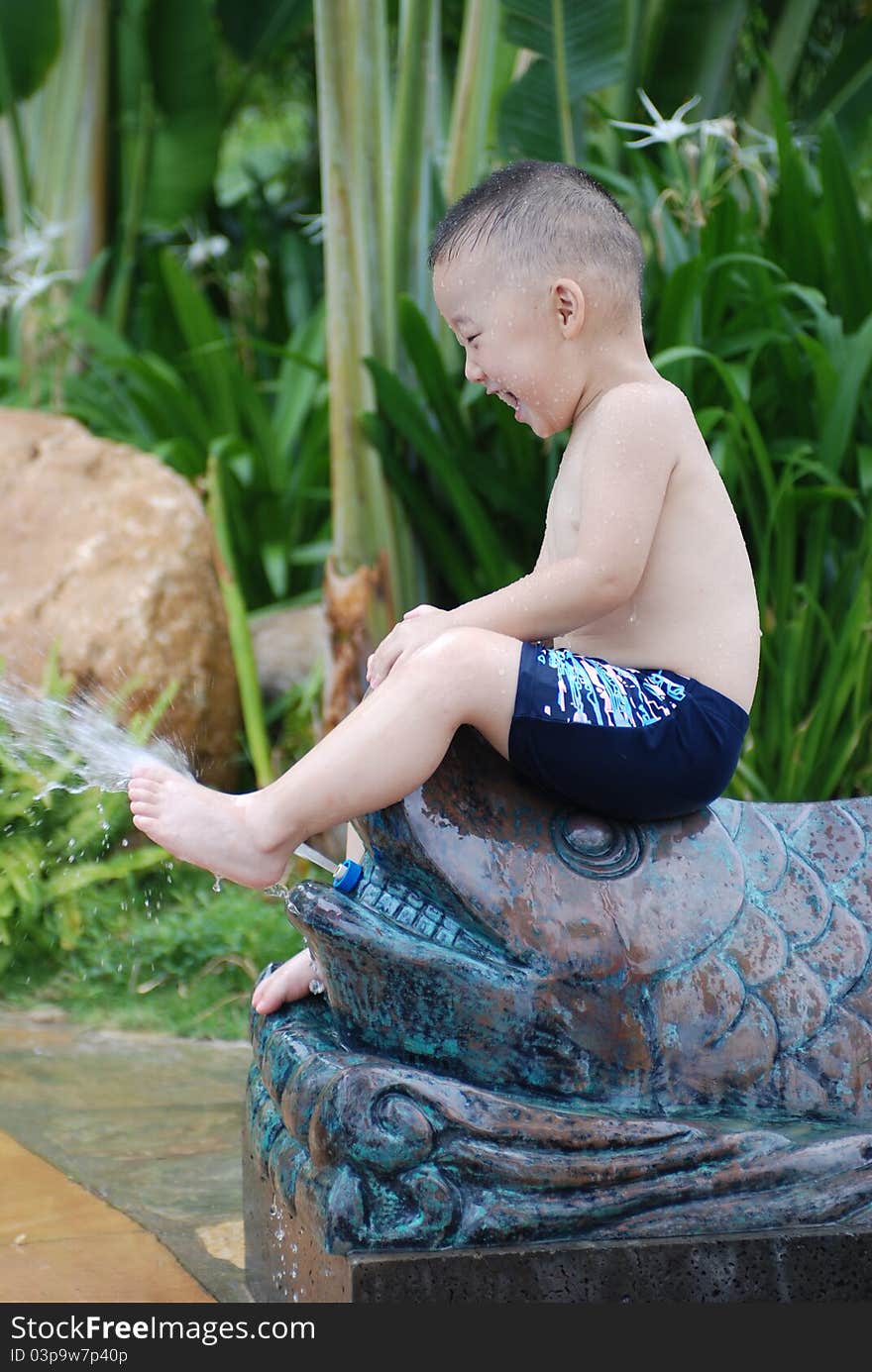 Little boy plays with water jet from fish-shape hose outdoors. Little boy plays with water jet from fish-shape hose outdoors