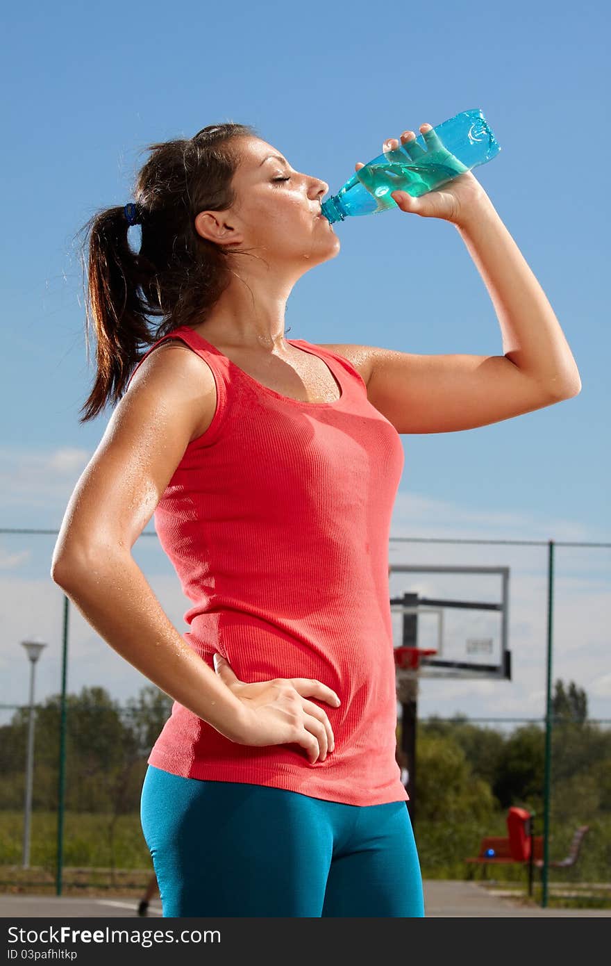 Young woman drinking mineral water on a basketball court. Young woman drinking mineral water on a basketball court