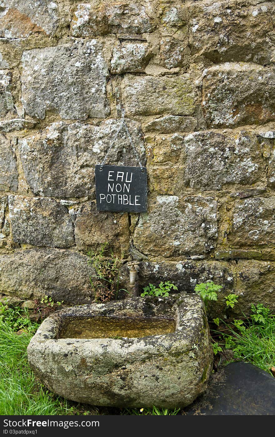 A French sign above an old basin and tap. A French sign above an old basin and tap