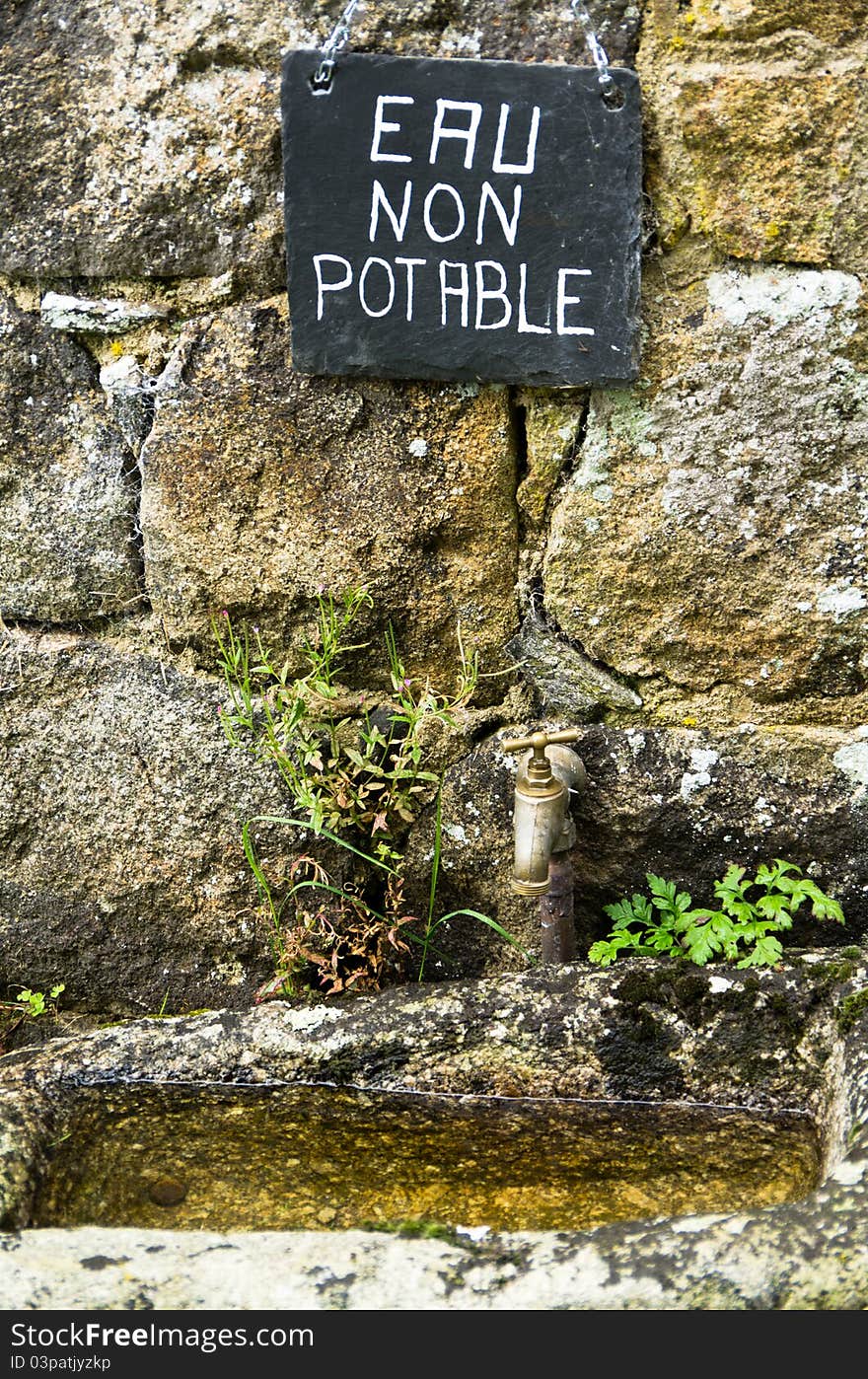 A French sign above an old basin and tap. A French sign above an old basin and tap