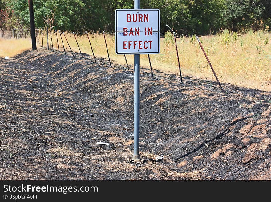 Burn ban sign in charred drainage ditch in central Texas during drought.