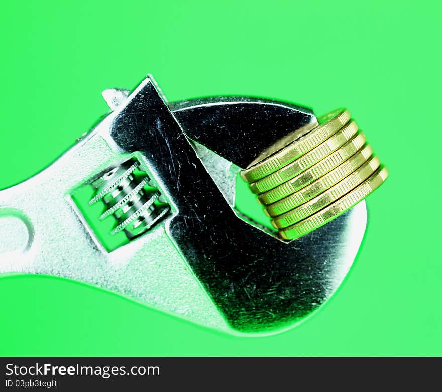 A stack of Gold Dollar Coins being squeezed in a silver adjustable spanner, against a light green background and asking the questions how tightly is your household budge being squeezed?. A stack of Gold Dollar Coins being squeezed in a silver adjustable spanner, against a light green background and asking the questions how tightly is your household budge being squeezed?