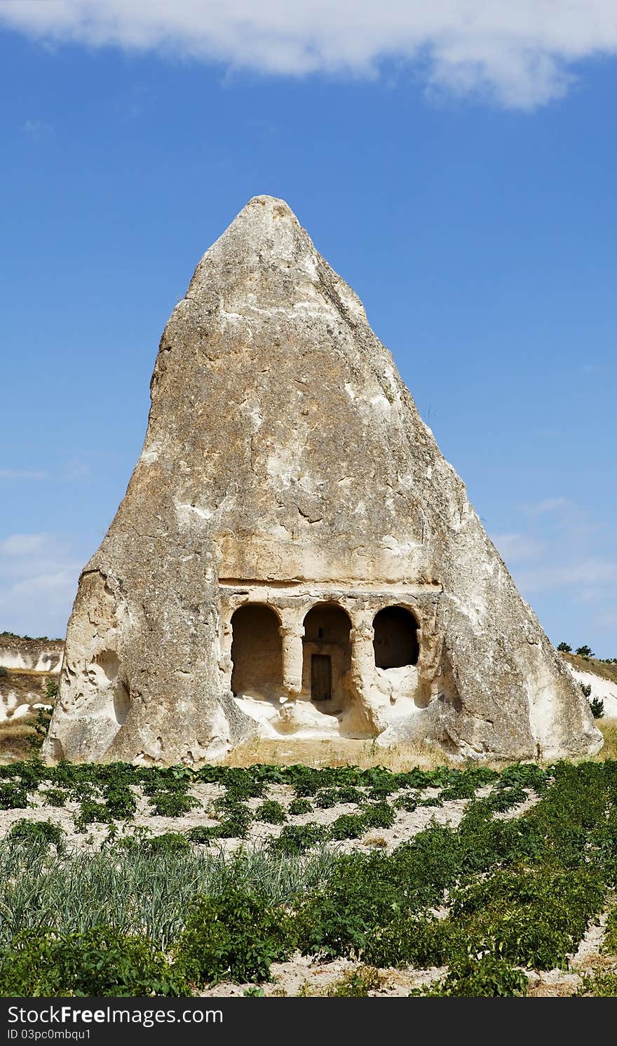 Old dis-used church carved from a limestone fairy chimney surrounded by arable land and farmed with potato crops, blue sky, layer of cloud, portrait, crop space and copy space. Old dis-used church carved from a limestone fairy chimney surrounded by arable land and farmed with potato crops, blue sky, layer of cloud, portrait, crop space and copy space