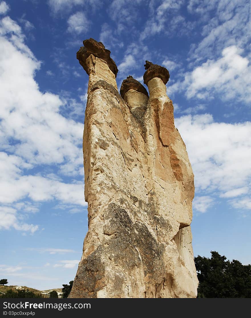 Foot to top group of three fairy chimney of Cappadocia, Turkey, portrait, crop space, copy space with blue cloudy sky, tree tops and hills. Foot to top group of three fairy chimney of Cappadocia, Turkey, portrait, crop space, copy space with blue cloudy sky, tree tops and hills