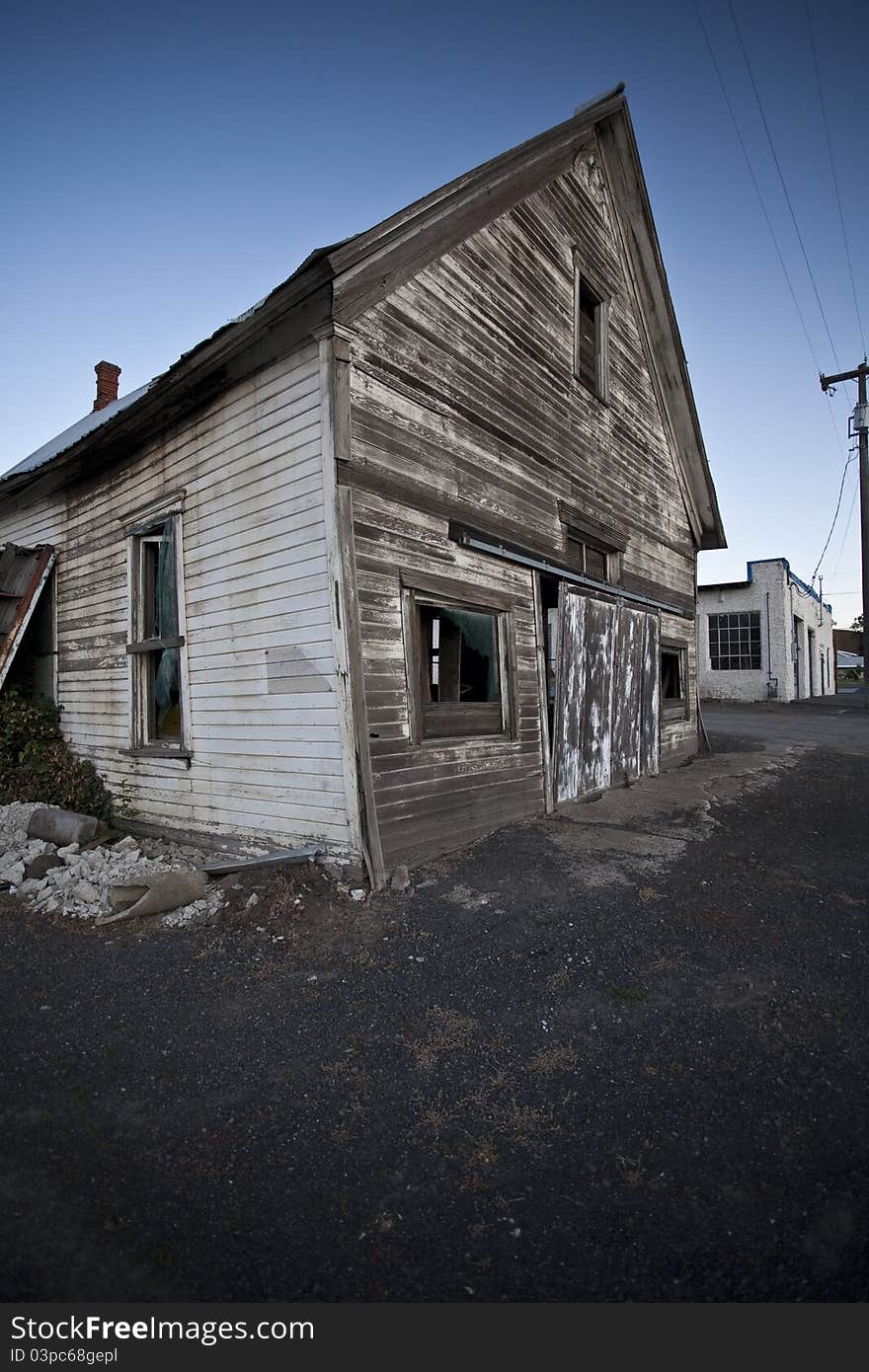 An aging and abandoned building sits in a nearly empty lot in the evening hours.