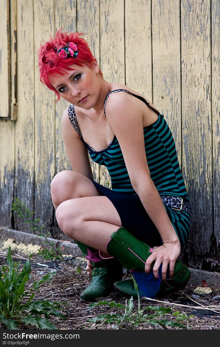 Young woman dressed in punk clothing with bright red hair in urban setting. Young woman dressed in punk clothing with bright red hair in urban setting