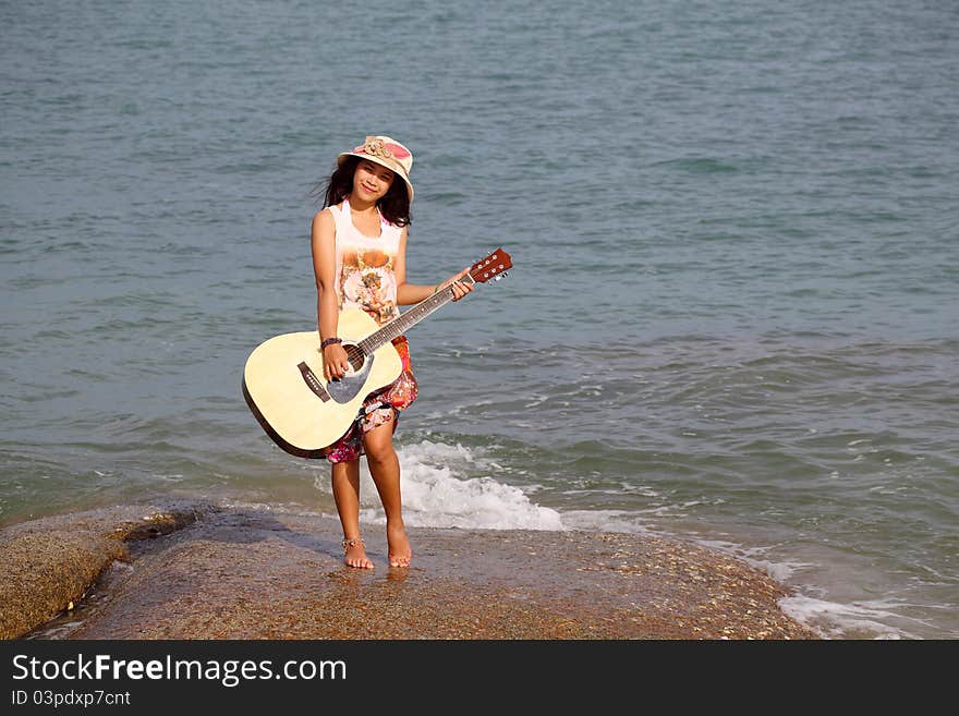 Pretty young woman with guitar on stone near beach