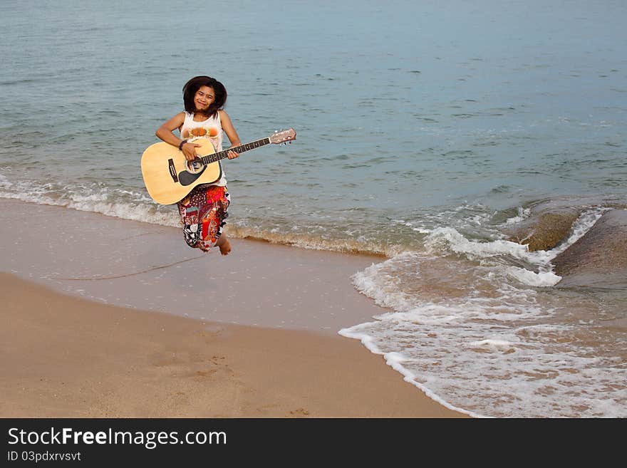 Happy girl jumping with guitar on beach