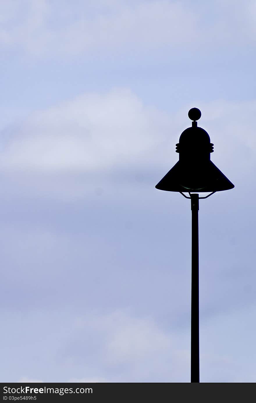 A street lamp silhouette againt a slightly overcast blue sky.