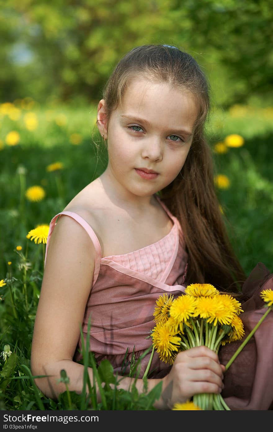 Little girl sits on a glade with dandelions