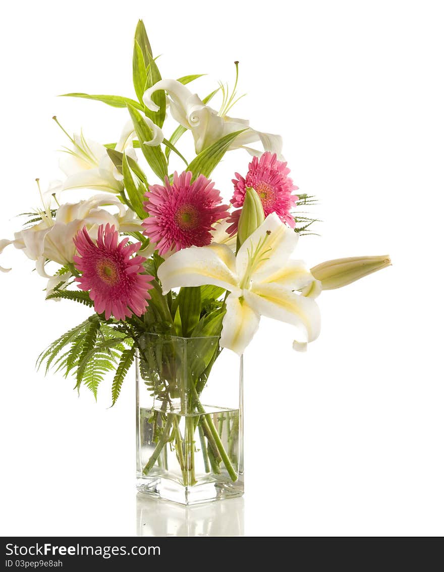 A bunch of lilies and gerberas in the transparent vase on the white background