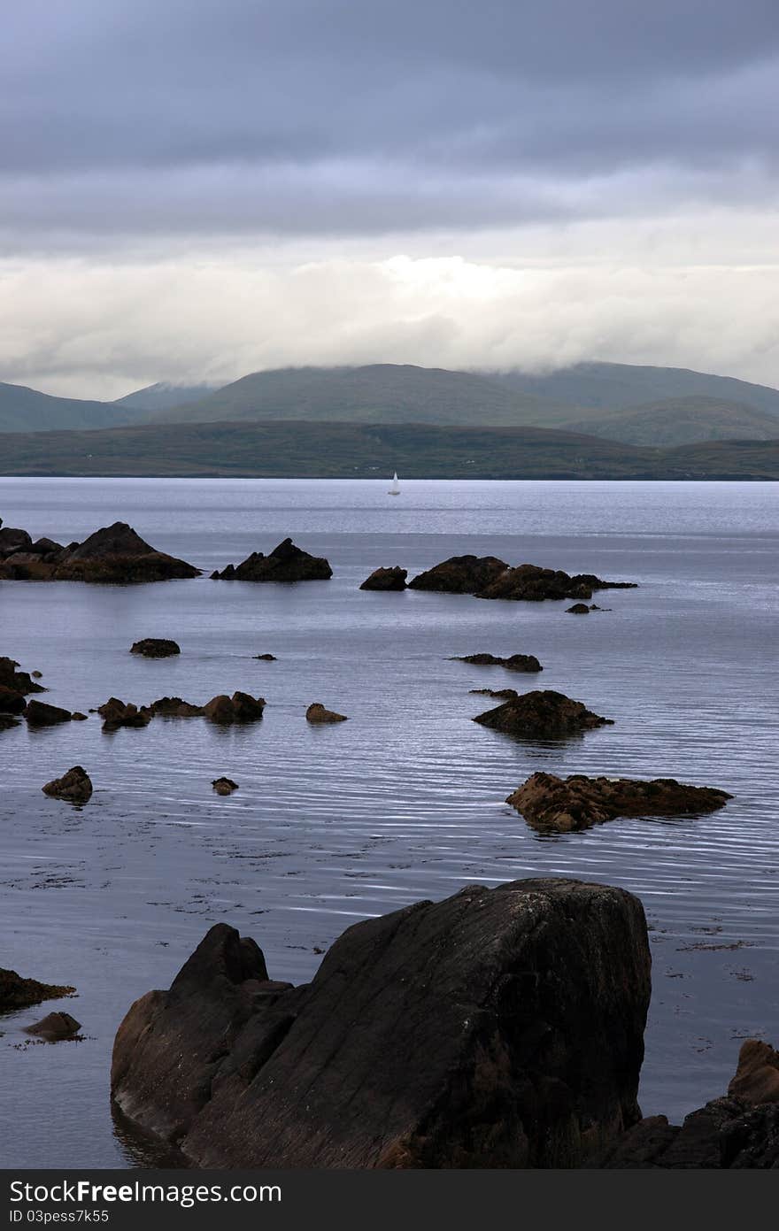 Scenic view in kerry ireland of lone yacht sailing in rocks and sea with mountains against a beautiful cloudy sky. Scenic view in kerry ireland of lone yacht sailing in rocks and sea with mountains against a beautiful cloudy sky