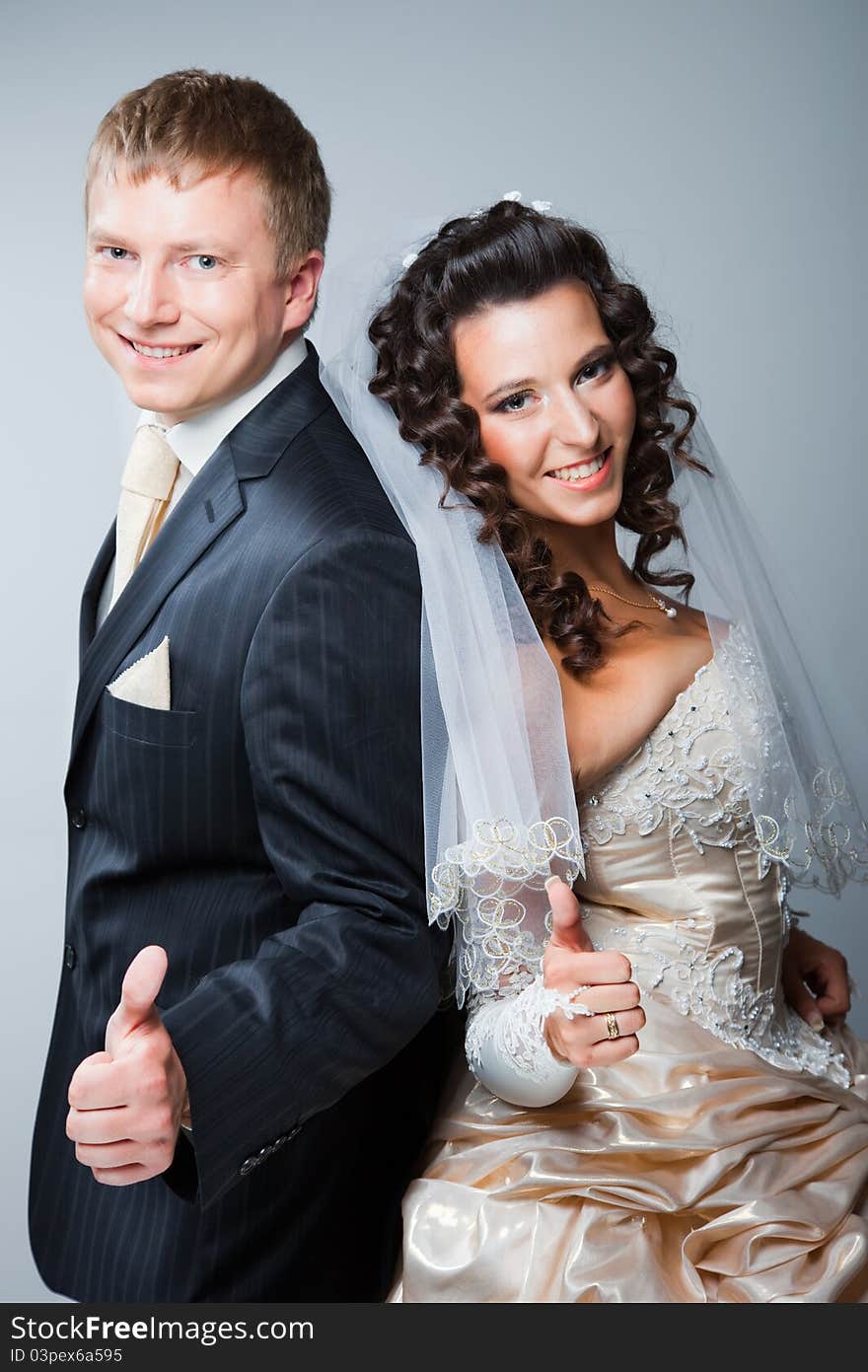 Studio portrait of young beautiful happy just married bride and groom gesticulating on gray background. Studio portrait of young beautiful happy just married bride and groom gesticulating on gray background