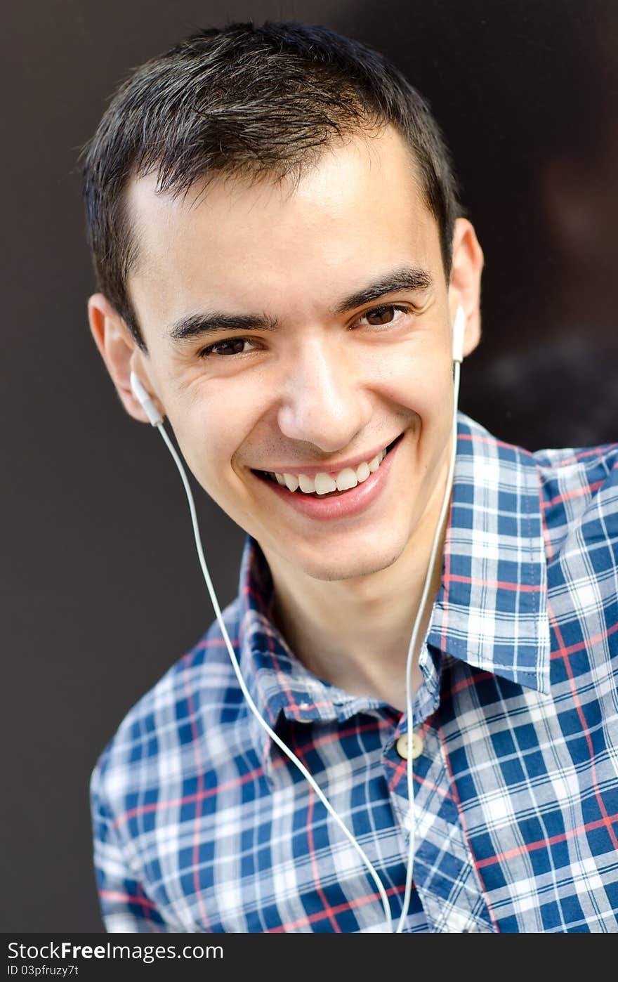 Portrait of handsome young man leaning casual on wall outside listening to music and smiling. Portrait of handsome young man leaning casual on wall outside listening to music and smiling