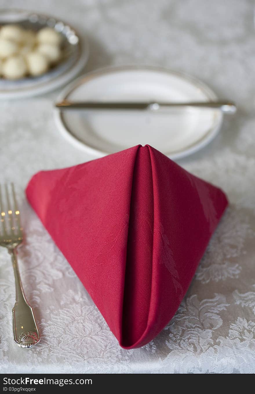 A folded red napkin and place setting are prepared for a diner.