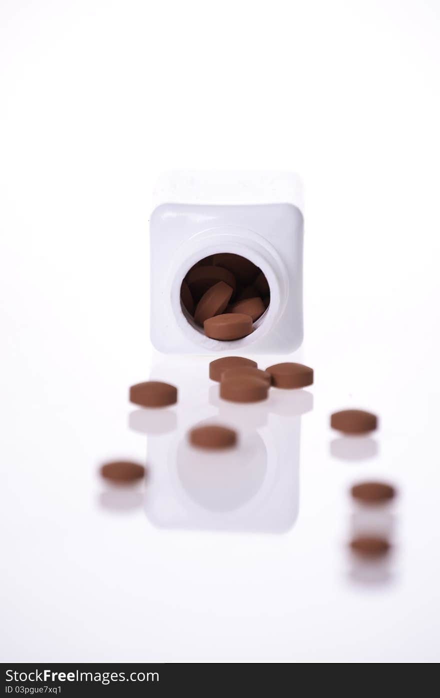 The inside of a white pill bottle with red generic pills on a white background. The inside of a white pill bottle with red generic pills on a white background.