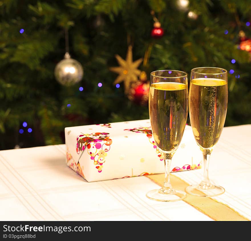 Two wine glasses with a present behind them and a christmas tree in the background. Two wine glasses with a present behind them and a christmas tree in the background