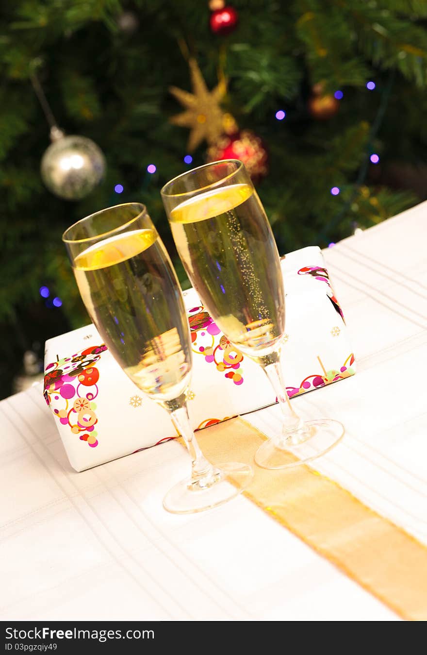 Two wine glasses with a present behind them and a christmas tree in the background. Two wine glasses with a present behind them and a christmas tree in the background