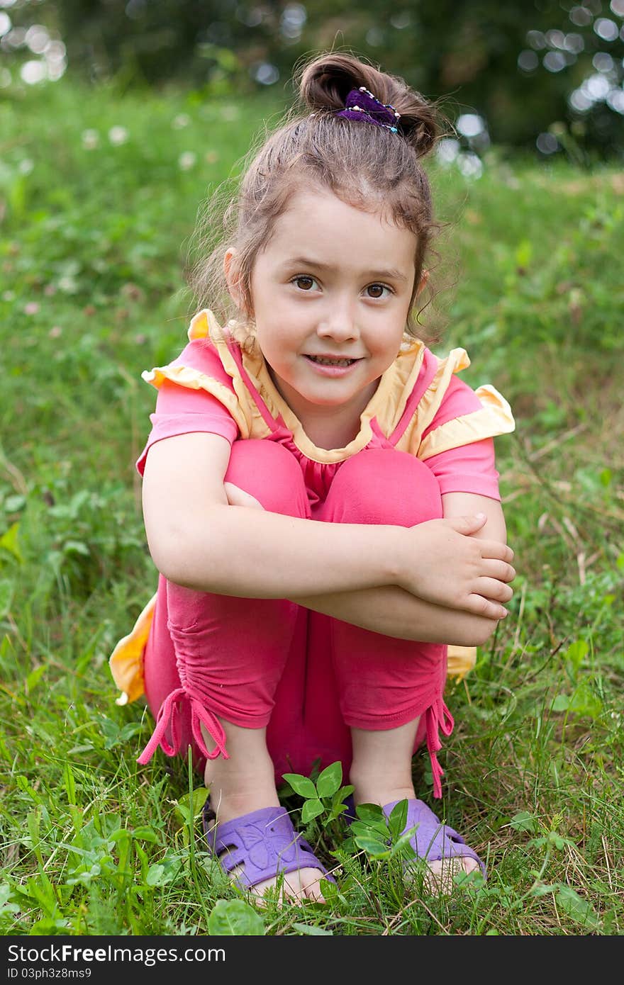 The little girl sits on a grass having drawn in knees. The little girl sits on a grass having drawn in knees