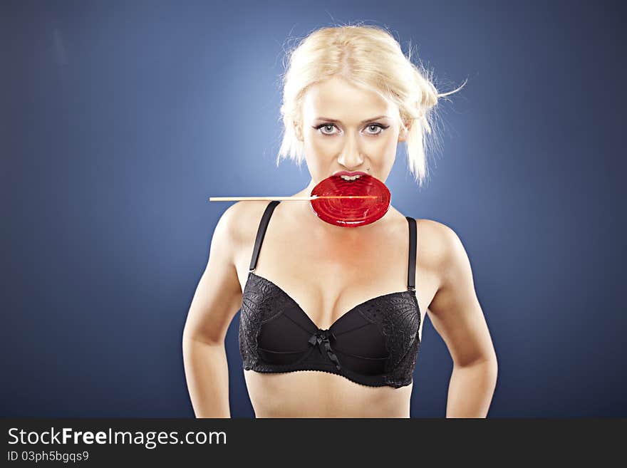 Beautiful blonde model bites into a red lollipop.