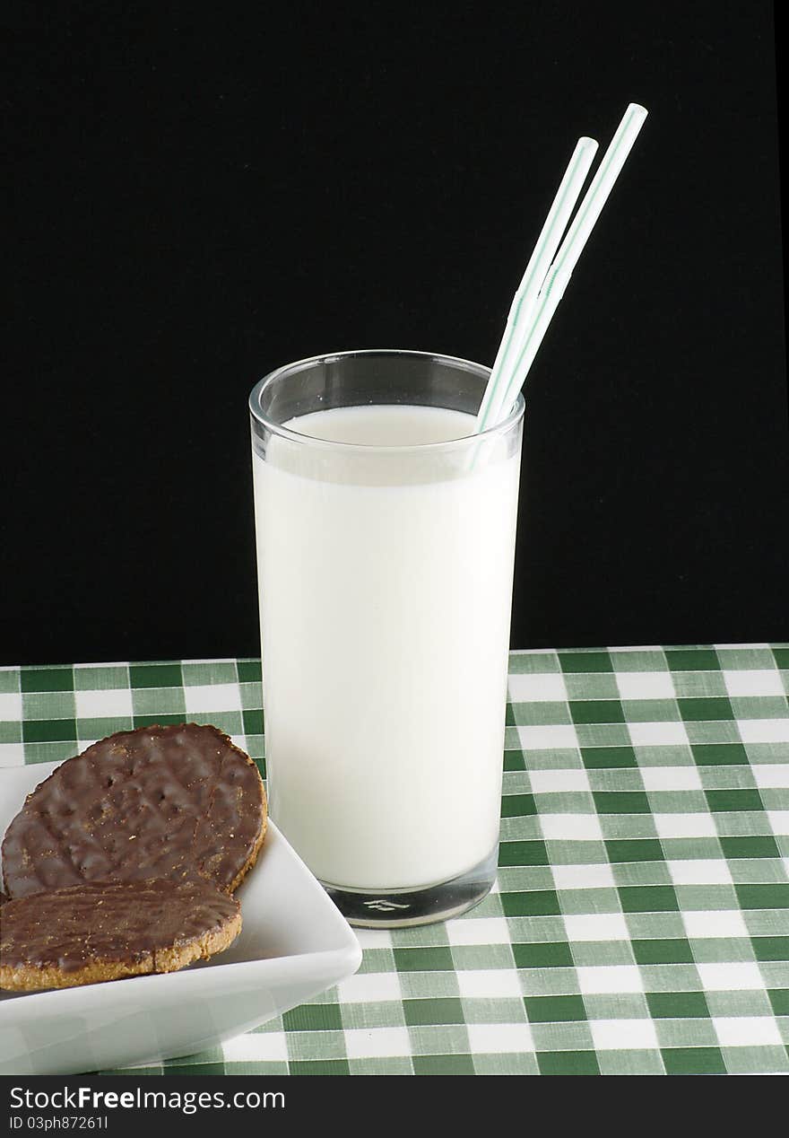 Glass of milk with chocolate coated cookies or biscuits on green gingham cloth. Glass of milk with chocolate coated cookies or biscuits on green gingham cloth