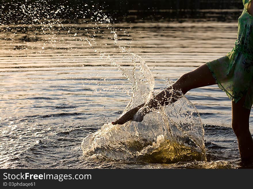 Young woman splashing the water in sunset lights