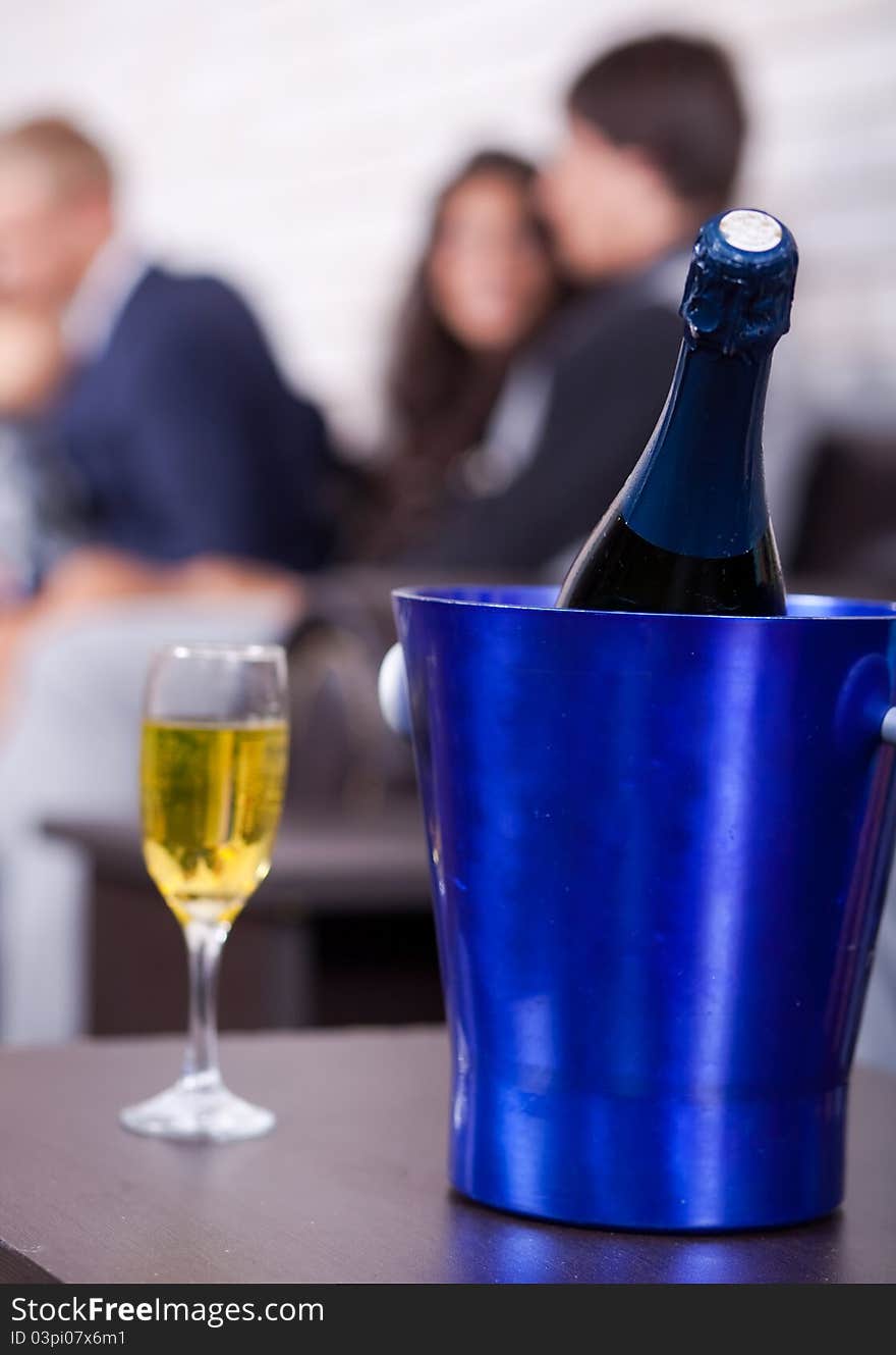 Champagne bottle in focus with glass filled, couples in background. Champagne bottle in focus with glass filled, couples in background