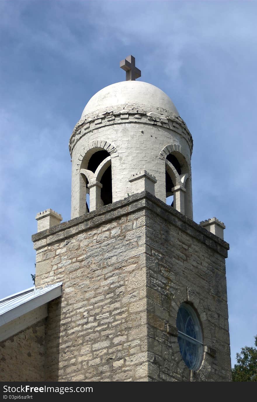 A stone and brick church tower with a cross reaches towards the blue sky.