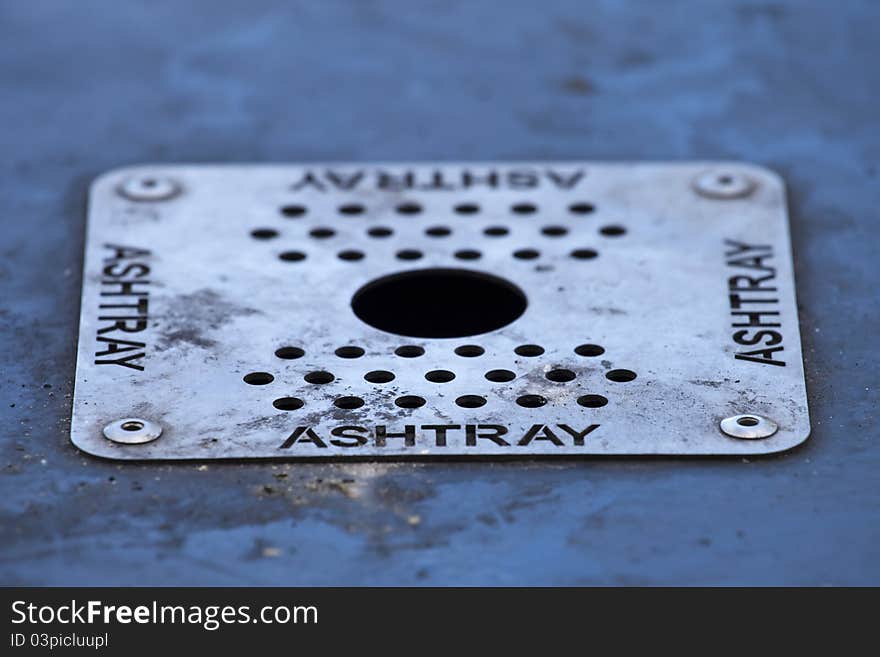 A dirty ashtray mounted on a public waste bin