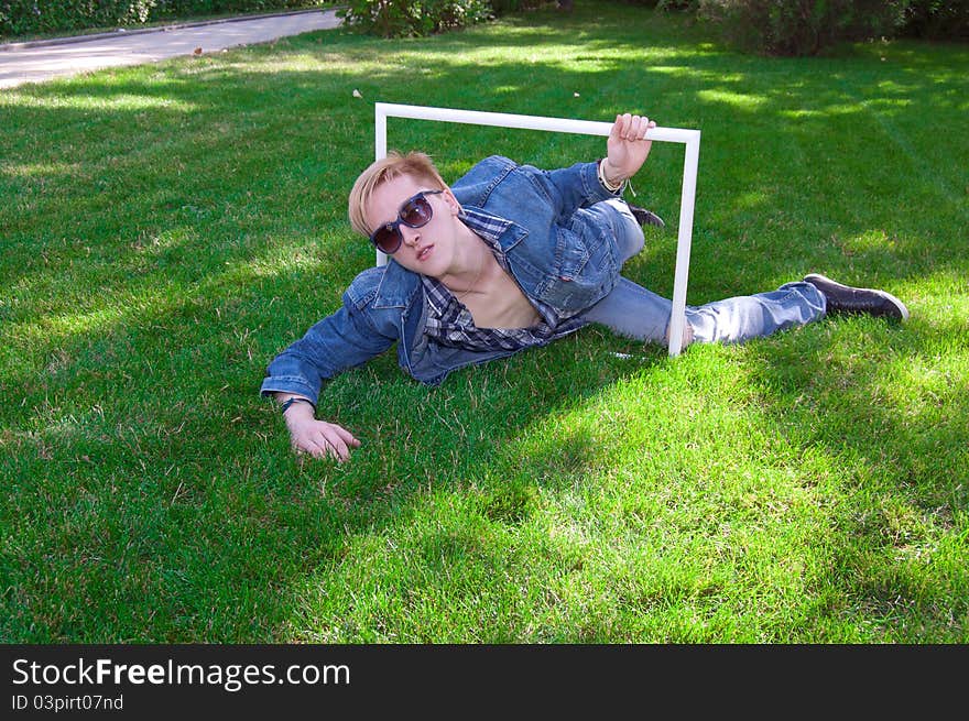 Young human on the green grass, he is wear jeans jacket, he has white frame and goggles. Young human on the green grass, he is wear jeans jacket, he has white frame and goggles