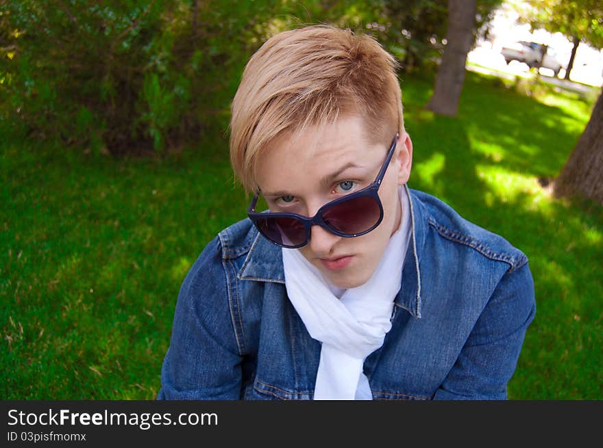 Young human on the green grass, he has blue goggles, jean jacket and white scarf