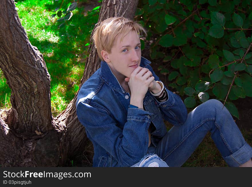 Young man in denim jacket relaxing by tree, summer scene. Young man in denim jacket relaxing by tree, summer scene.