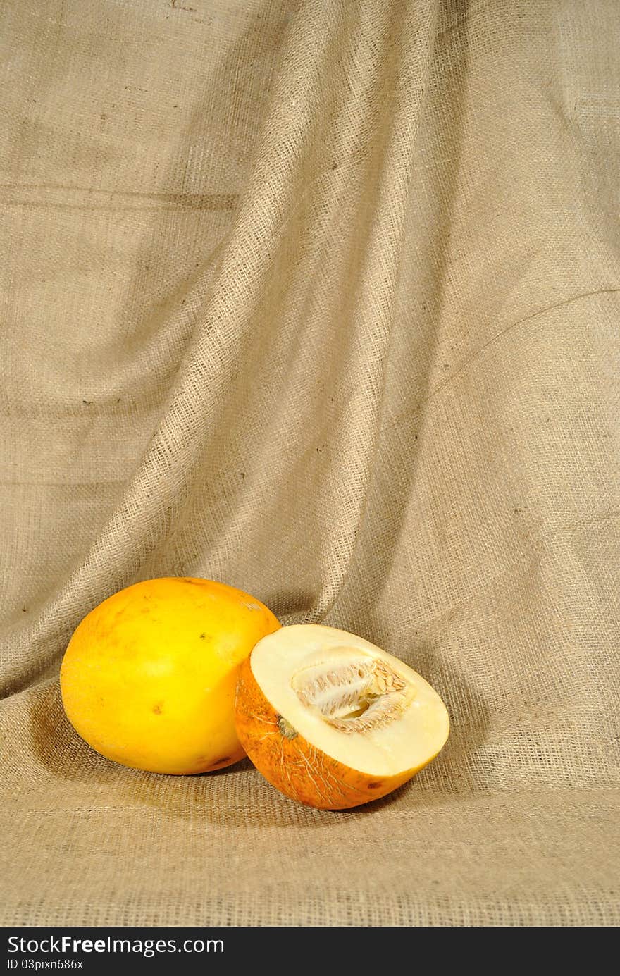 The autumn topic. In the foreground are two orange melons. One of them are cuted in half. They lie on the table covered by rough stuff. This staff creates background so. The autumn topic. In the foreground are two orange melons. One of them are cuted in half. They lie on the table covered by rough stuff. This staff creates background so.