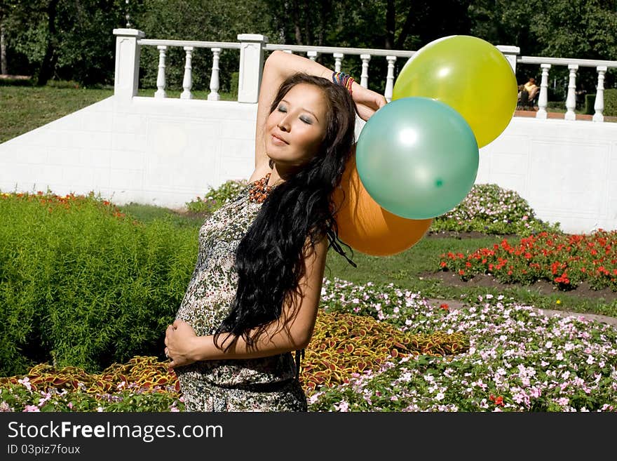 Joyful pregnant girl with colorful balloons walking in park