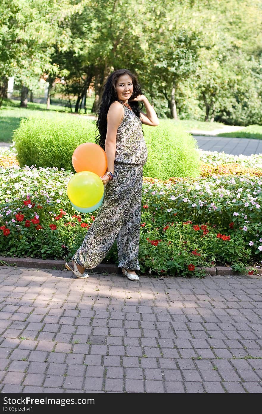 Joyful pregnant girl with colorful balloons walking in park. Joyful pregnant girl with colorful balloons walking in park