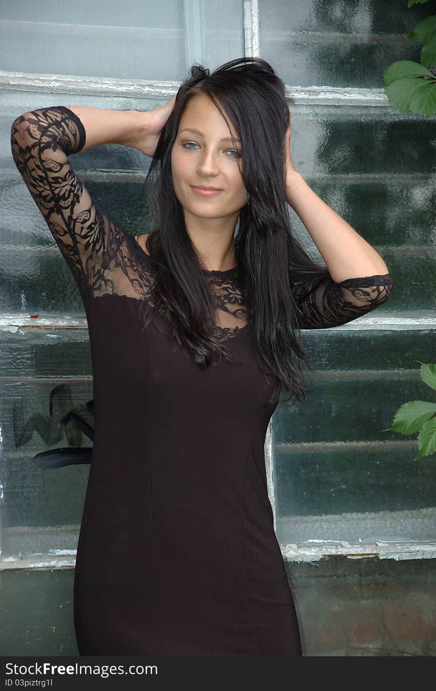 Female model wearing black dress. Girl with confident smile, standing near old window. Female model wearing black dress. Girl with confident smile, standing near old window.