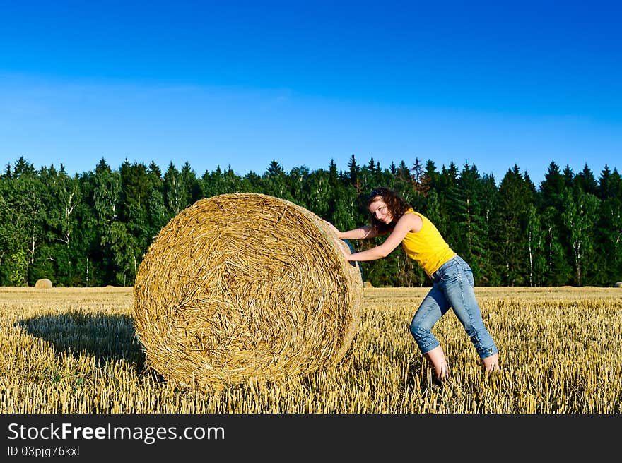 Funny girl rolls a haystack in a field. Russia, Moscow region