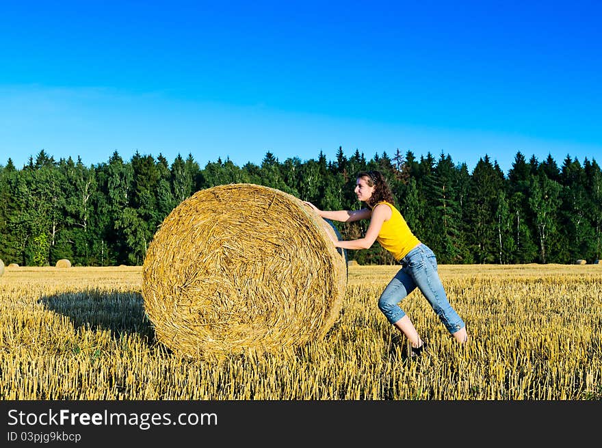 Funny girl rolls a haystack in a field