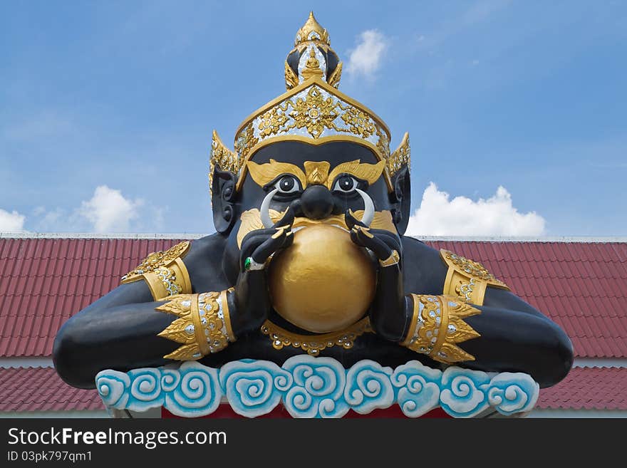 Statue of black deity called Rahu and blue sky background.