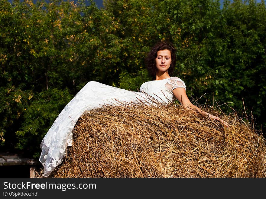 Brunette woman in white dress on hay in the woods